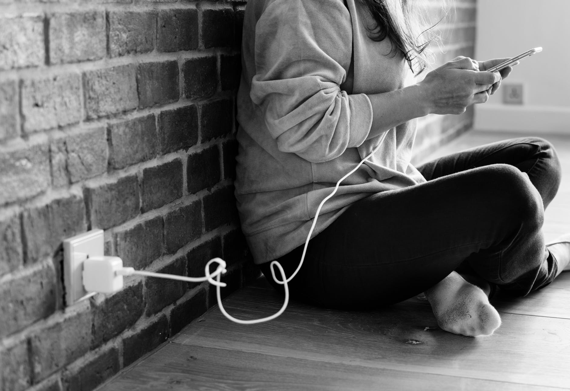 grayscale photography of person using smartphone while charging